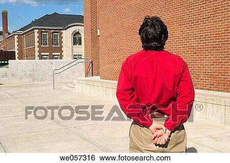 Stock Photograph - Man, his hands behind his back, standing outside on a concrete walkway. Fotosearch