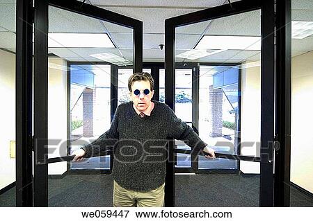 Man in an office building, wearing blue sunglasses, holding open the lobby doors View Large Photo Image Stock Photo - Man in an office building, wearing blue sunglasses, holding open the lobby doors. Fotosearch