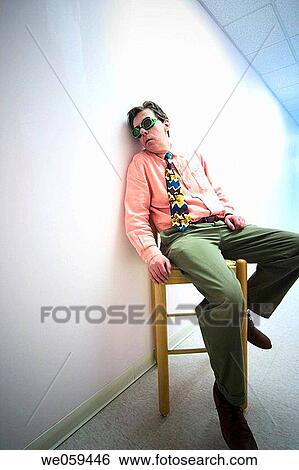 Stock Photograph - Man wearing goggles and a tie, sitting in a chair next to a white wall. Fotosearch