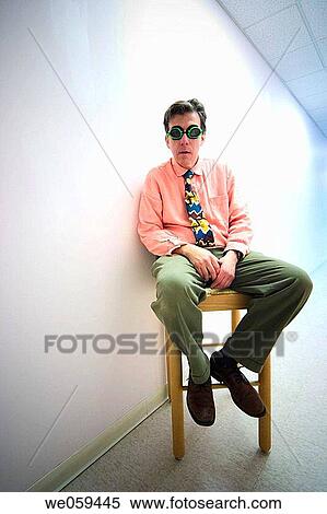 Man wearing goggles and a tie, sitting in a chair next to a white wall View Large Photo Image Stock Photography - Man wearing goggles and a tie, sitting in a chair next to a white wall. Fotosearch