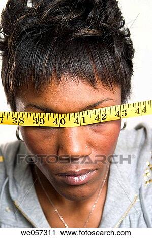 Young black woman holding a tape measure against her face View Large Photo Image Stock Image - Young black woman holding a tape measure against her face. Fotosearch