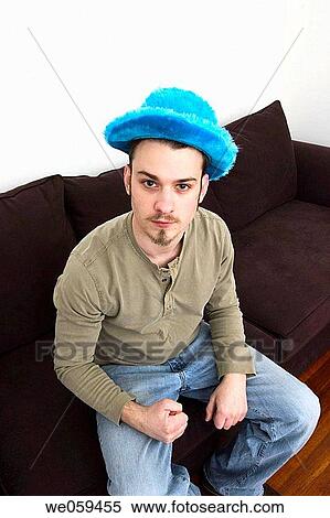 Young man, wearing a blue hat and sitting on a sofa, making a fist View Large Photo Image Stock Photography - Young man, wearing a blue hat and sitting on a sofa, making a fist. Fotosearch