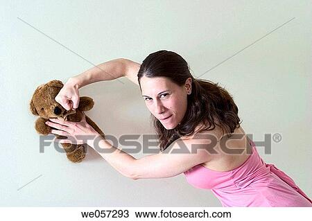 Stock Image - Young woman pretending to punch a stuffed animal. Fotosearch