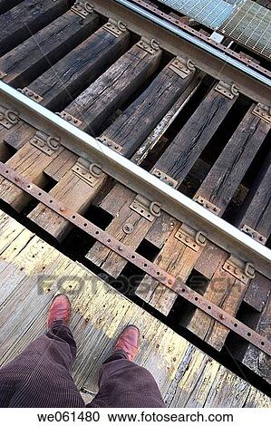 Stock Image - Close_up of a man's legs and feet standing next to railroad tracks. Fotosearch