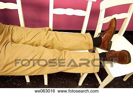 Close_up of a man's legs and feet resting on two chairs View Large Photo Image Stock Photograph - Close_up of a man's legs and feet resting on two chairs. Fotosearch