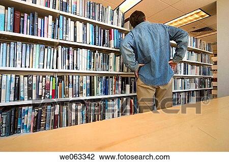 Man standing in front of a bookshelf at a library. View Large Photo Image Stock Image - Man standing in front of a bookshelf at a library.. Fotosearch