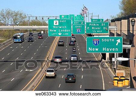 Stock Image - Traffic signs and automobiles on a stretch of highway going through a city.. Fotosearch