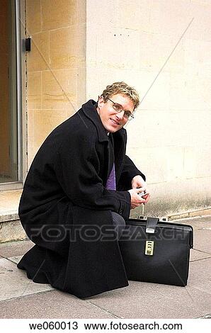 Stock Image - Young businessman outside office with mobile phone and briefcase. Shot in Bath, United Kingdom.. Fotosearch