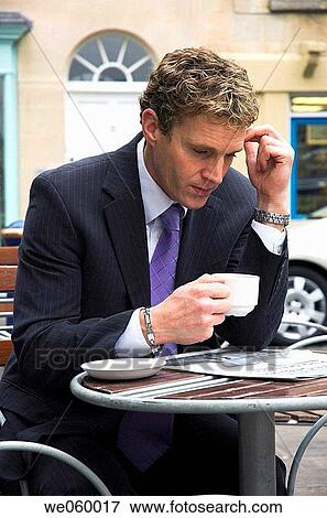 Stock Photo - Young businessman sitting outside at a cafe with a newspaper. Shot in Bath, United Kingdom.. Fotosearch