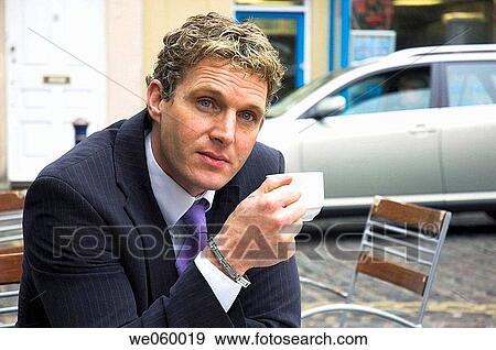 Stock Photo - Young businessman sitting outside at a cafe with a newspaper. Shot in Bath, United Kingdom.. Fotosearch