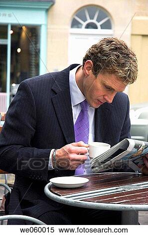 Stock Photography - Young businessman sitting outside at a cafe with a newspaper. Shot in Bath, United Kingdom.. Fotosearch