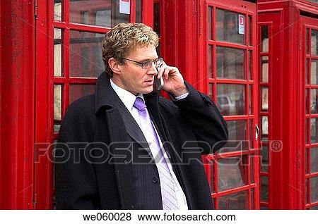 Young businessman talking on a mobile phone next to a row of British red phone boxes. View Large Photo Image Stock Photo - Young businessman talking on a mobile phone next to a row of British red phone boxes.. Fotosearch