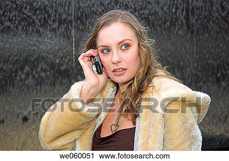 Stock Image - Young female fashion model wearing a fur coat and using a mobile phone.. Fotosearch