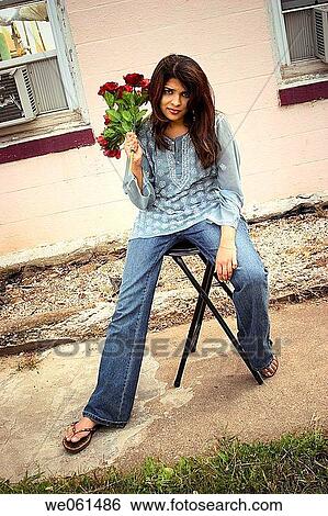 Stock Photograph - Young Indian woman, holding a bouquet of flowers, posing in front of an old motel. Fotosearch