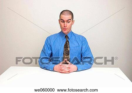 Young man in business shirt and tie sitting at an empty desk. Expression suggests surprise and nervousness, at an unusual request perhaps. View Large Photo Image Stock Image - Young man in business shirt and tie sitting at an empty desk. Expression suggests surprise and nervousness, at an unusual request perhaps.. Fotosearch