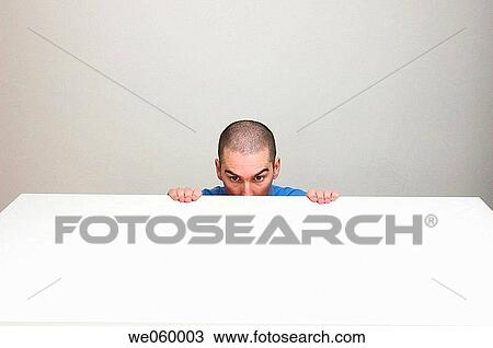 Young man in business shirt crouching behind an empty desk. His expression suggests nervousness about something. View Large Photo Image Stock Image - Young man in business shirt crouching behind an empty desk. His expression suggests nervousness about something.. Fotosearch