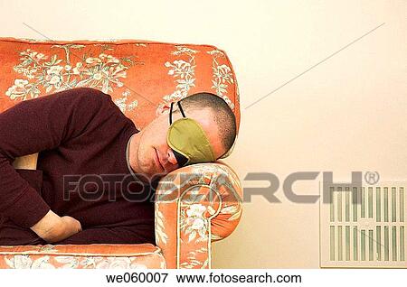 Young man wearing eye mask catching up on some sleep on a floral sofa. View Large Photo Image Stock Photo - Young man wearing eye mask catching up on some sleep on a floral sofa.. Fotosearch