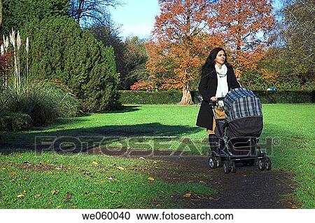 Young woman pushing a pram walking through a park. View Large Photo Image Stock Image - Young woman pushing a pram walking through a park.. Fotosearch