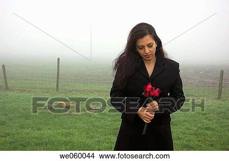 Young woman standing with roses on a cold misty winter morning. View Large Photo Image Picture - Young woman standing with roses on a cold misty winter morning.. Fotosearch