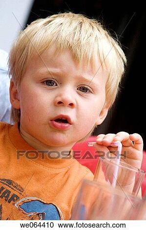Stock Image - 3 year old boy sitting in a cafe drinking through a straw looking into camera. Fotosearch