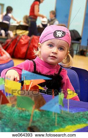 Stock Image - 3 year old girl at a pirate party, with a pretend treasure island, wearing a bandanna. Fotosearch