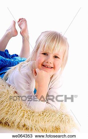 Stock Image - 3 year old girl lying on the studio floor, smiling into camera. Fotosearch