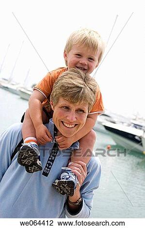 Stock Image - 40 year old woman, with her son on her shoulders, smiling off camera. Fotosearch