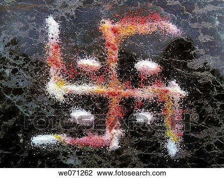Stock Image - A holy sign called swastik, in Hindu Religion is made by colorful powder which is made from pounding particular soft stones during festal ceremony. This type of drawing is called as Rangoli, which is usually in graphic form. Maharashtra, India.. Fotosearch