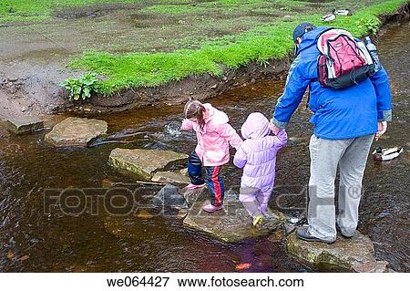 Stock Photo - father helping his 2 little girls across stepping stones over a river. Fotosearch