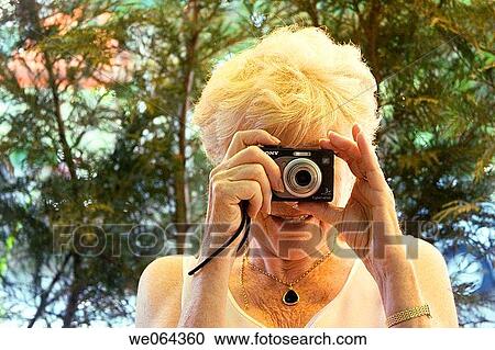 Stock Image - glamorous, 70 year old lady taking a photo of the photographer, smiling. Fotosearch