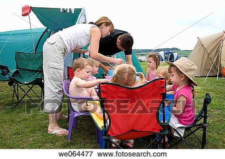 Stock Photo - group of children sitting round a table eating tea on a camping trip with a man and a woman helping them. Fotosearch