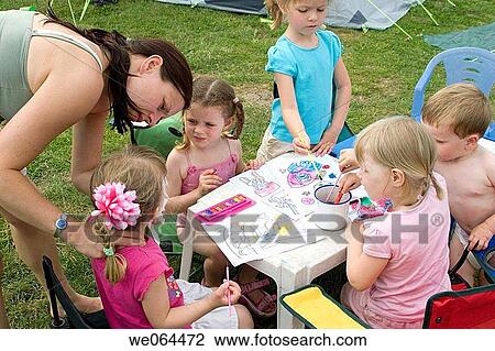 group of five children sitting round a table painting on a camping trip, with one of the mothers helping View Large Photo Image Stock Image - group of five children sitting round a table painting on a camping trip, with one of the mothers helping. Fotosearch