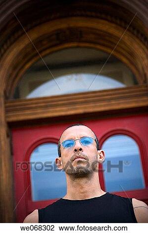 Hispanic man, wearing blue sunglasses, standing in front of an office building View Large Photo Image Stock Image - Hispanic man, wearing blue sunglasses, standing in front of an office building. Fotosearch