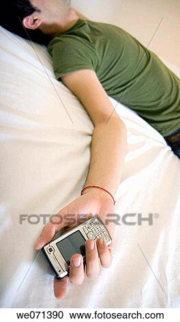 Man laying on bed holding cell phone View Large Photo Image Stock Image - Man laying on bed holding cell phone. Fotosearch