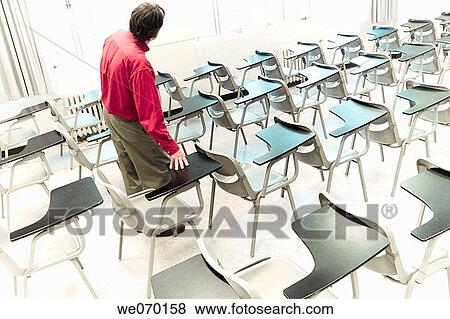Man Standing Among Student Desks In An Empty College Classroom