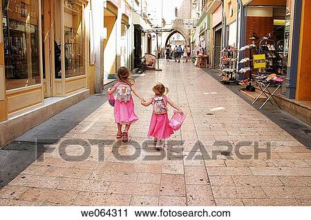 Stock Image - the back of 2 sisters age 3 aAND 5, walking down a narrow street in Apt, France. Fotosearch