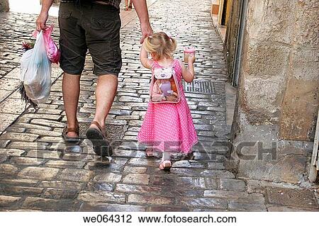 the back of a father walking down a cobbled street holding his daughters hand View Large Photo Image Stock Image - the back of a father walking down a cobbled street holding his daughters hand. Fotosearch