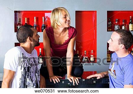 Stock Image - Two men looking at woman on bar counter. Fotosearch