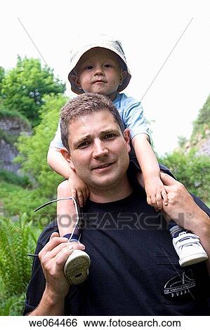 Stock Photograph - two year old boy sitting on his fathers shoulders both looking into camera. Fotosearch