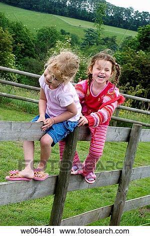Stock Image - two young children playing on a fence smiling into camera. Fotosearch