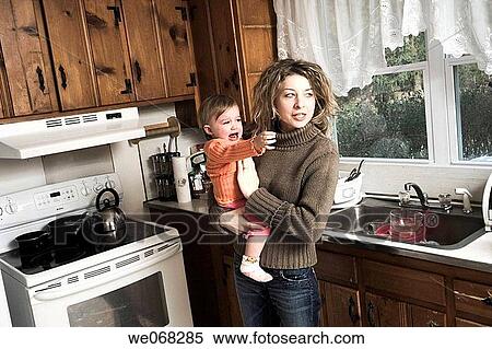 Woman, standing in her kitchen, holding her young daughter View Large Photo Image Stock Photography - Woman, standing in her kitchen, holding her young daughter. Fotosearch