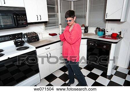 Picture - Woman, wearing sunglasses, posing in her kitchen. Fotosearch