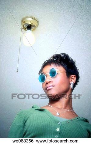 Young black woman, wearing sunglasses, standing underneath a light fixture View Large Photo Image Stock Photograph - Young black woman, wearing sunglasses, standing underneath a light fixture. Fotosearch