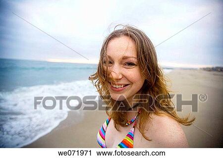 Stock Image - 20 year old woman smiles as the breeze blows her hair at dusk on a Pacific ocean beach in Los Angeles, California, USA. Fotosearch