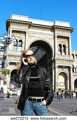 Stock Photography - 29 year old woman using cell phone in front of Galleria Vittorio Emanuelle II, Piazza del Duomo, Milan. Lombardy, Italy. Fotosearch