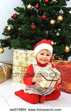 Child wearing Father Christmas hat with presents in front of Christmas Tree View Large Photo Image Picture - Child wearing Father Christmas hat with presents in front of Christmas Tree. Fotosearch