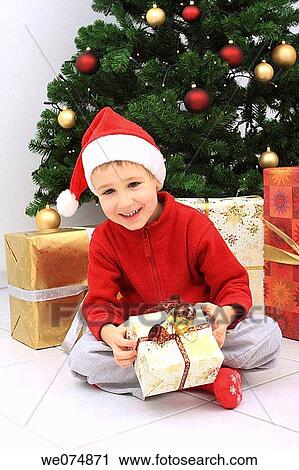 Child wearing Father Christmas hat with presents in front of Christmas Tree View Large Photo Image Stock Image - Child wearing Father Christmas hat with presents in front of Christmas Tree. Fotosearch