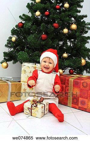 Stock Photography - Child wearing Father Christmas hat with presents in front of Christmas Tree. Fotosearch