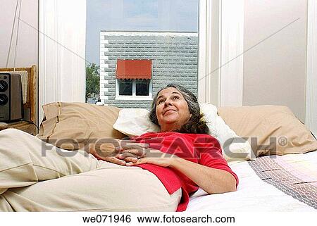 Elderly woman rests comfortably on bed by window. View Large Photo Image Stock Photograph - Elderly woman rests comfortably on bed by window.. Fotosearch