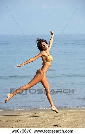 Stock Image - Latin girl jumping on the beach. Fotosearch